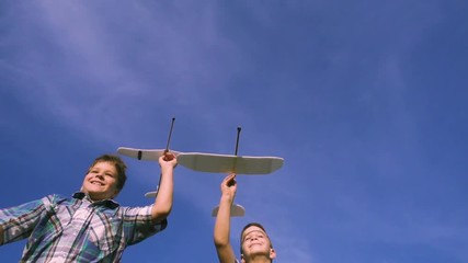 Two boys running with airplanes against blue sky