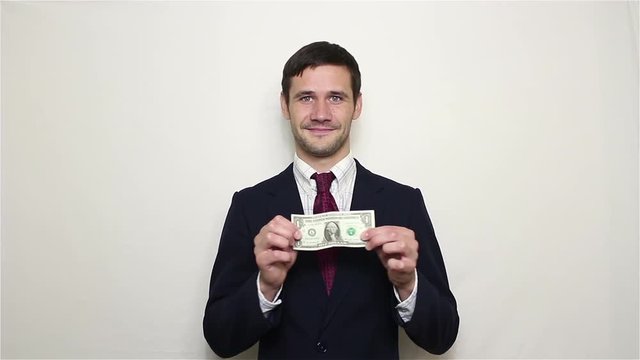 Young handsome businessman shows one dollar and verifies its authenticity by stretching to the sides.Portrait on white background