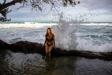 woman sitting on rock and water from the ocean hits the rock