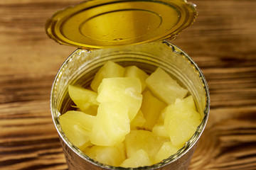 Opened tin can of pineapple pieces on wooden table