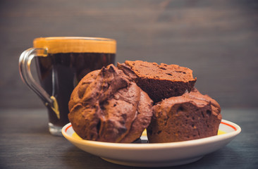 Chocolate muffins on a plate and a cup of coffee are photographed on a black wooden background.