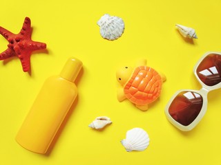 Yellow sunscreen bottle, seashells, rubber toy turtle, sunglasses and seashells. Flat lay beach essentials 
