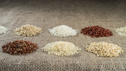 Several heaps of rice of different varieties on the background of sacking. Selective focus.