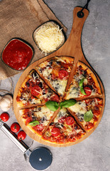 Vegetarian Italian pizza with melted cheese, red tomatoes and green basil on a table decorated by cheese, tomato and cherry tomatoes