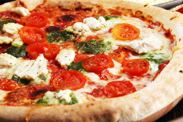 Pizza with tomatoes, mozzarella cheese, black olives and basil. Delicious italian pizza on wooden pizza board.