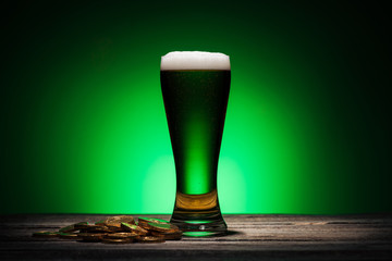 glass of green beer near golden coins on st patricks day on green background