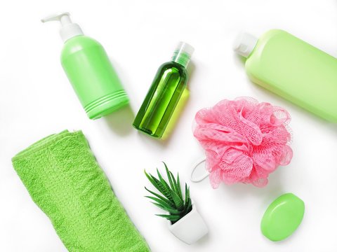Green liquid soap, essential oil, shampoo, rolled cotton towel, pink sponge. Flat lay herbal organic natural bath products and spa cosmetics for skin, hair care
