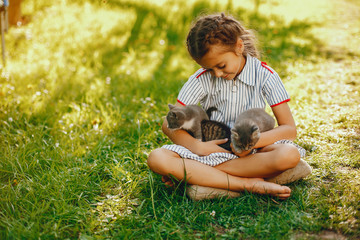 beautiful and cute girl in blue dresses with beautiful hairstyles and make-up sitting in a sunny green garden and playing with a cats