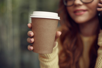 Young lady holding take-away hot drink on blurred background