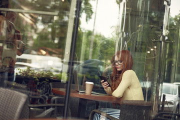 Beautiful young lady with hot drink using cellphone in cozy cafe