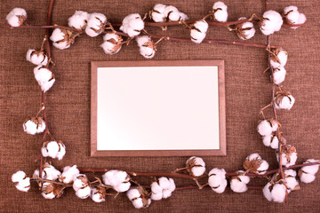 Frame with fluffy dried cotton bolls over rough brown burlap. Top view, copy space, greeting card