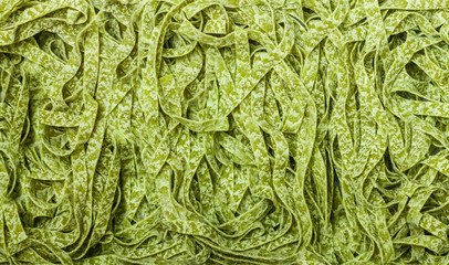 Raw homemade Italian green pasta spinach tagliatelle close up. Dry noodles. Culinary background. Selective focus, top view