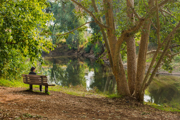 Obraz premium Woman sitting on a bench near lake background.