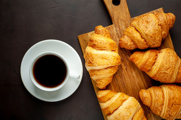 coffee and croissants on wooden cutting board, on the background concrete