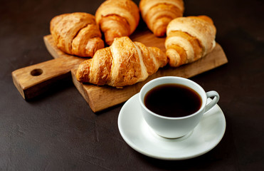 coffee and croissants on wooden cutting board, on the background concrete