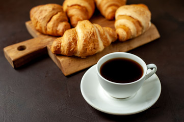 coffee and croissants on wooden cutting board, on the background concrete