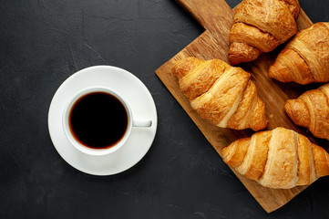 coffee and croissants on wooden cutting board, on the background concrete
