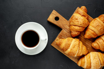 coffee and croissants on wooden cutting board, on the background concrete