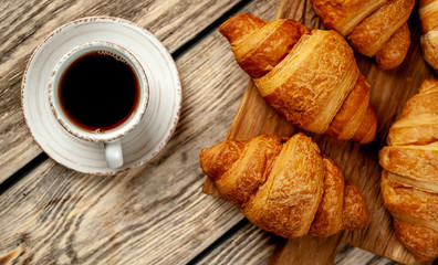 coffee and croissants on wooden cutting board, on wooden background