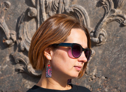 Attractive woman in bright tribal earrings and sunglasses near vintage wall in baroco style.