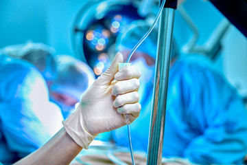 Dropper into a vein close-up on a background of the surgical operational. Doctor woman in sterile gloves sets the drip