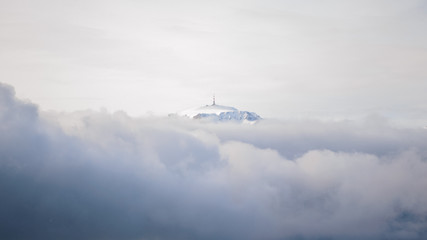 Fototapeta na wymiar Mountain peak with a TV/radio relay on top, as seen above the clouds, on a cloudy Winter day with atmospheric inversion - Costila in Bucegi mountains, Romania, as seen from Baiului mountains