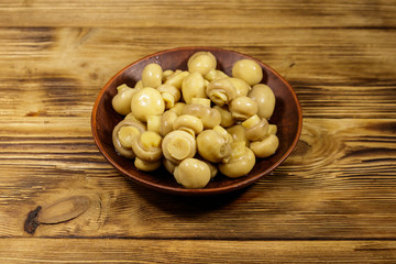 Ceramic plate with pickled champignons. Marinated mushrooms on wooden table