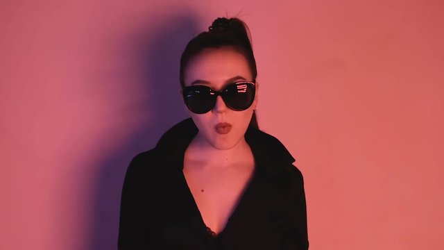 Brunette in neon lights. A woman in sunglasses and a black jacket looks into the camera. HD