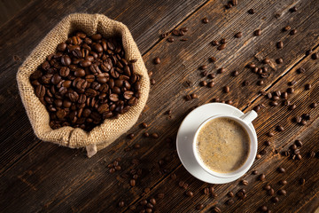 Coffee cup with coffee seeds on vintage wood table and sag of beans form the top.