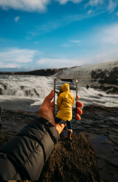 D montage of man taking smartphone picture of Iceland's landscape and woman wearing yellow raincoat