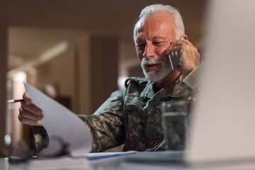 Smiling senior sergeant reading documents and talking on mobile phone.