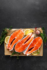 Fresh raw salmon fish steaks on black background with ingredients for cooking. Closeup. Top view