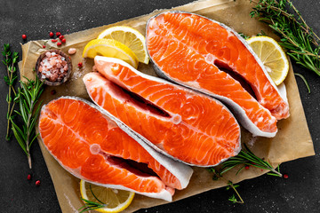 Fresh raw salmon fish steaks on black background with ingredients for cooking. Closeup. Top view