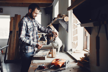 A man carves a tree. The carpenter works in a studio. Boy with cute dog