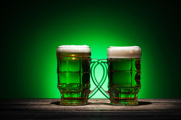 glasses of irish ale standing on wooden table on green background