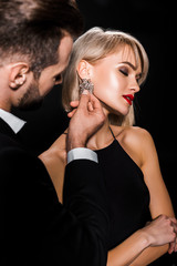 man touching elegant earrings of attractive woman isolated on black