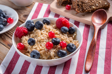 Close up view of porridge with blueberries and raspberries and grain bread on wooden background. Vegan breakfast.