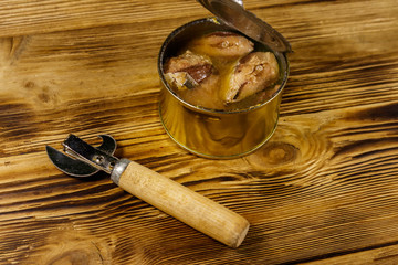 Open tin can of sardine fish and can opener on wooden table