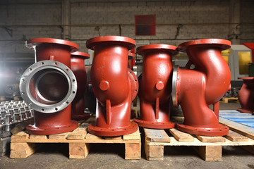 Large metal or cast iron pipes, bases for creating valves, lie on a wooden panel before further...