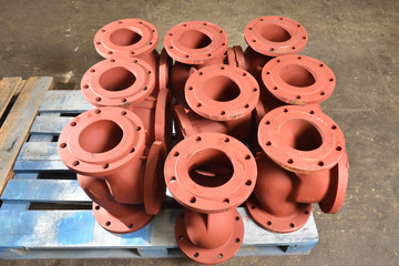 Iron or cast iron pipes, bases for creating valves, lie on a wooden panel before further processing...