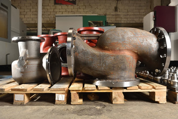 Large-sized metal or cast-iron pipes, bases for creating valves, lie on a wooden panel before further processing on a milling machine. Very big base not painted to create valves in the factory