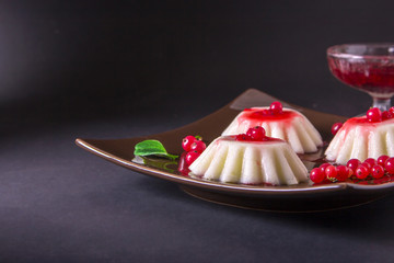 Semolina pudding in a brown square plate with red currant syrup and berries. On a dark background