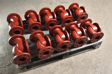 Red-colored metal pipes, bases for creating valves, lie on a wooden board after painting for...