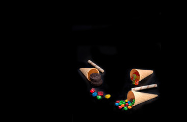 Multicolored dragee and gelatin sweets in a waffle cup on a black background