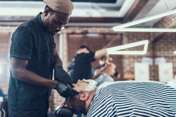Concentrated man shaving client with foam on face