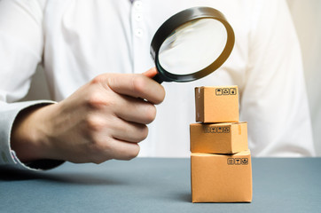 A man holds a magnifying glass above the boxes. Examination of goods for the presence of...