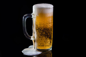 Cold beers with foam drops on black background. Pouring foam on the glass
