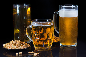Three glasses of beer and snack on a dark, black background.