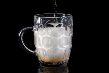Filling by beer a glass on a black background.