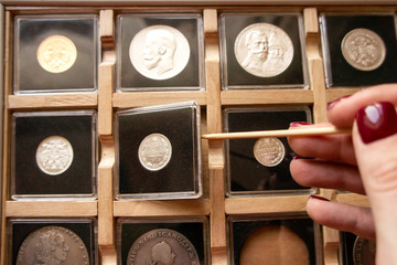 Female hand taking out a coin from a wooden display case with numismatic collection with a wooden...